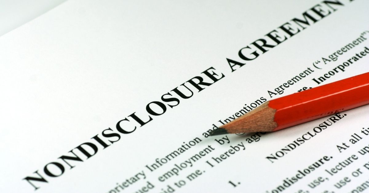 A professional close-up of a business professional signing a confidential Non-Disclosure Agreement (NDA) document on an office desk.